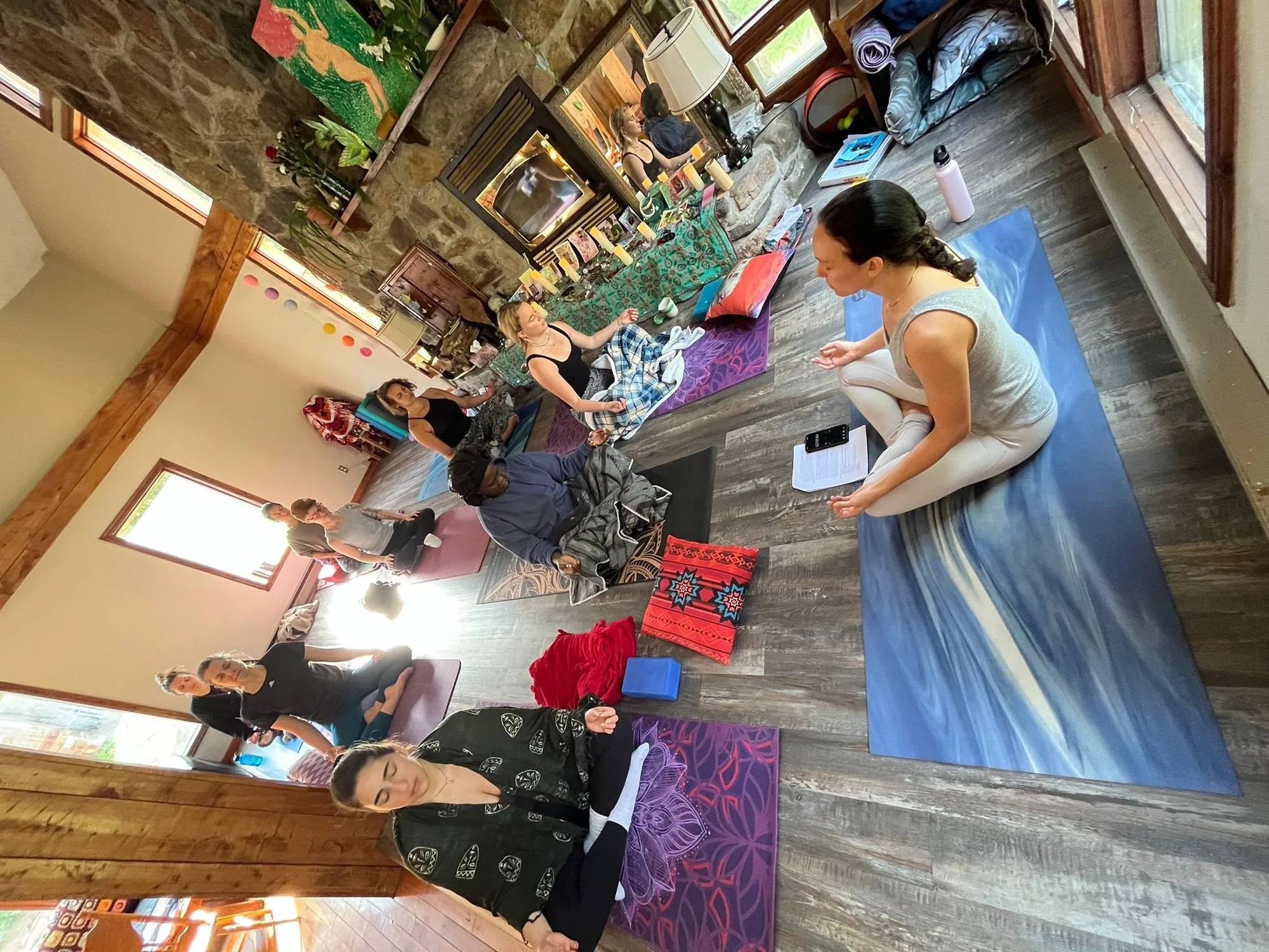 A group practising yoga on colourful mats in a sunlit room with a stone fireplace